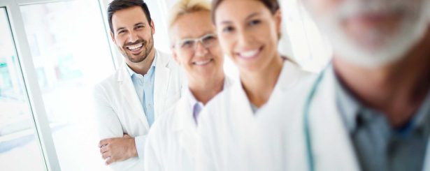 Closeup portrait of group of mixed age team of doctors in a line at a local hospital. There are two senior colleagues, and early 30's male and female colleagues. The man is in focus.